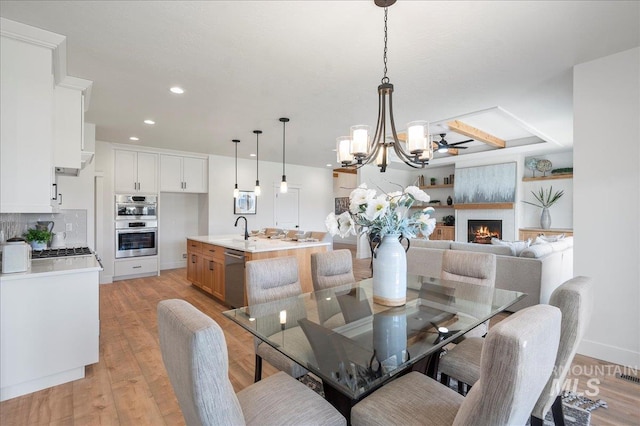 dining room with ceiling fan with notable chandelier, sink, a large fireplace, and light hardwood / wood-style flooring