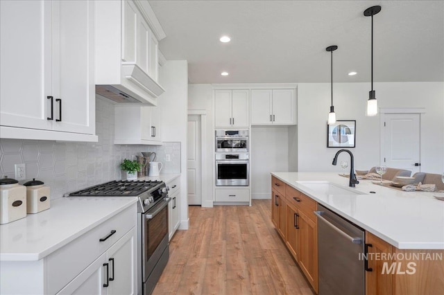 kitchen with appliances with stainless steel finishes, white cabinetry, a kitchen island with sink, and sink