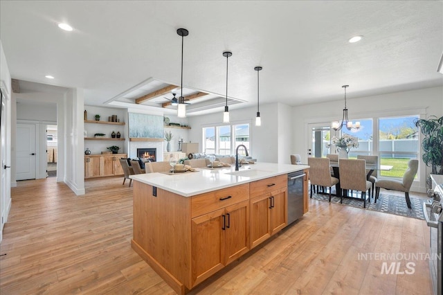 kitchen featuring sink, a large fireplace, stainless steel dishwasher, ceiling fan with notable chandelier, and a center island with sink