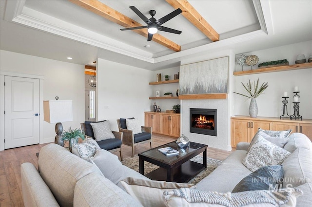 living room with beamed ceiling, ornamental molding, a large fireplace, ceiling fan, and light wood-type flooring