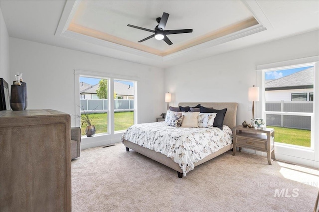 bedroom featuring light carpet, ceiling fan, and a tray ceiling