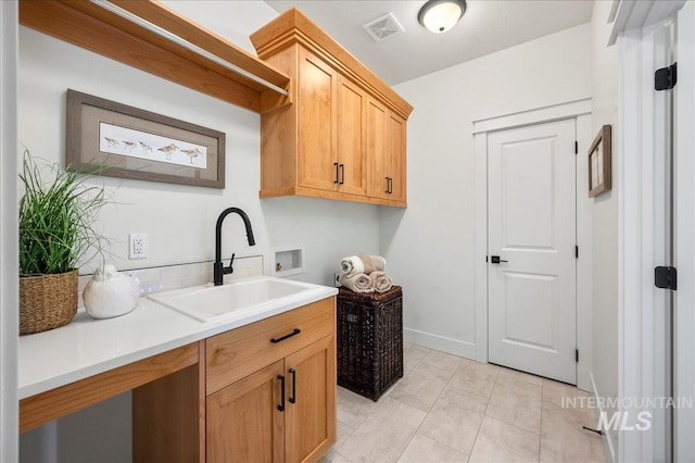 clothes washing area featuring sink, cabinets, light tile patterned floors, and washer hookup