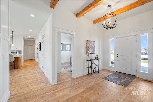 entryway with light hardwood / wood-style floors, an inviting chandelier, plenty of natural light, and beamed ceiling