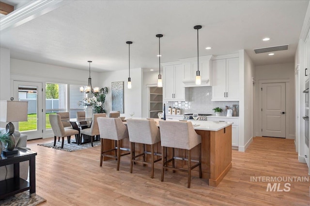 kitchen with white cabinetry, a chandelier, an island with sink, light hardwood / wood-style flooring, and tasteful backsplash