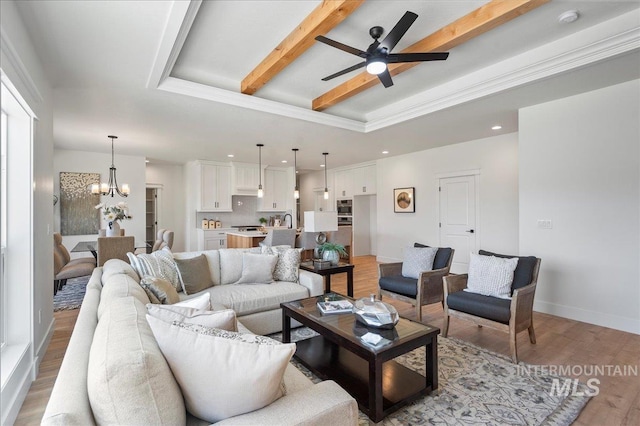 living room with ceiling fan with notable chandelier, light hardwood / wood-style floors, a tray ceiling, and beam ceiling