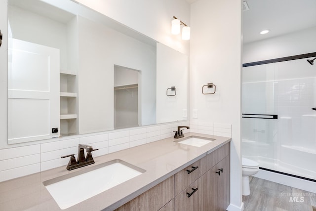 bathroom with toilet, a shower with shower door, wood-type flooring, vanity, and decorative backsplash