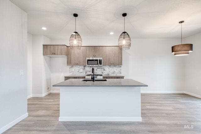 kitchen with backsplash, decorative light fixtures, an island with sink, and light wood-type flooring