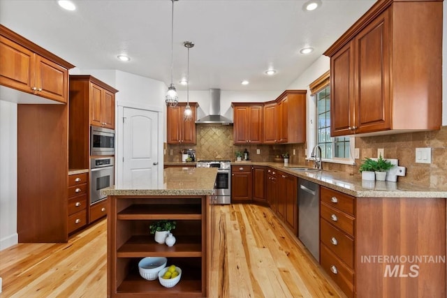 kitchen featuring a kitchen island, wall chimney range hood, appliances with stainless steel finishes, hanging light fixtures, and light hardwood / wood-style flooring