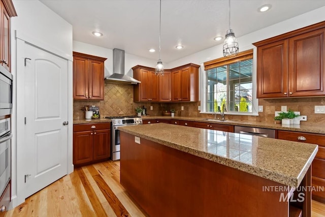 kitchen featuring stainless steel appliances, light hardwood / wood-style floors, wall chimney exhaust hood, a center island, and pendant lighting