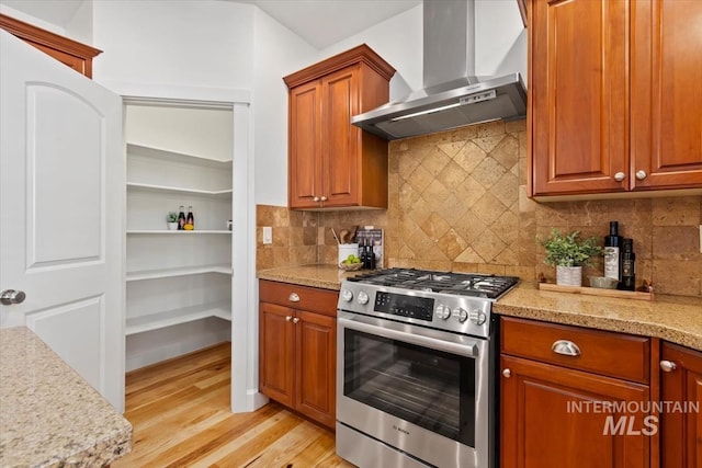 kitchen featuring light hardwood / wood-style floors, light stone counters, backsplash, wall chimney range hood, and stainless steel stove