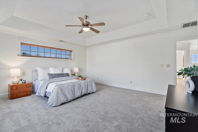 bedroom with light colored carpet, ceiling fan, multiple windows, and a tray ceiling