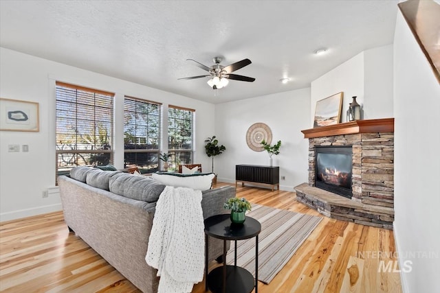 living room with light hardwood / wood-style floors, ceiling fan, a textured ceiling, and a stone fireplace