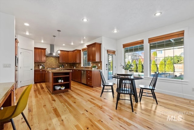 kitchen featuring a kitchen island, pendant lighting, light hardwood / wood-style floors, stainless steel dishwasher, and wall chimney exhaust hood