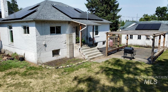 back of house with brick siding, roof mounted solar panels, a patio, a shingled roof, and a chimney