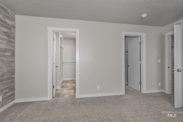 unfurnished bedroom featuring a walk in closet, light colored carpet, a textured ceiling, and a closet