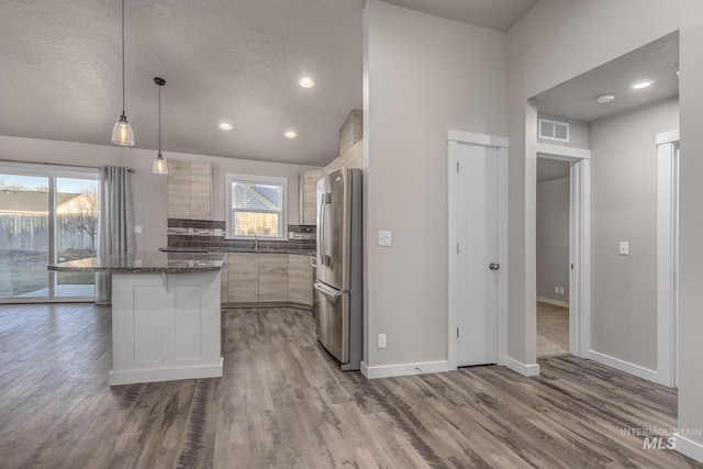 kitchen featuring pendant lighting, stainless steel refrigerator, backsplash, a kitchen bar, and hardwood / wood-style flooring