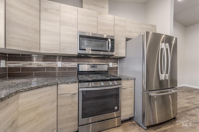 kitchen featuring light brown cabinets, dark stone counters, hardwood / wood-style flooring, stainless steel appliances, and decorative backsplash