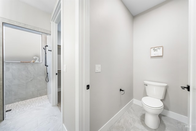 bathroom with toilet, marble finish floor, baseboards, and a tile shower