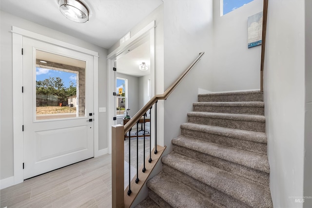 foyer with baseboards, stairway, and light wood-style flooring