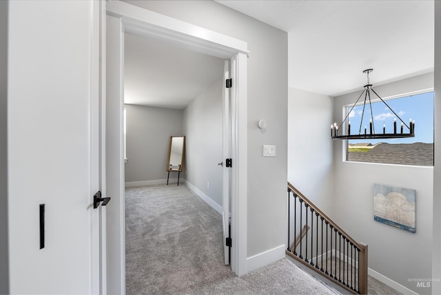 hallway featuring a chandelier, carpet floors, an upstairs landing, and baseboards