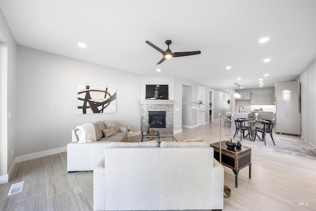 living room with a ceiling fan, baseboards, a tiled fireplace, and recessed lighting