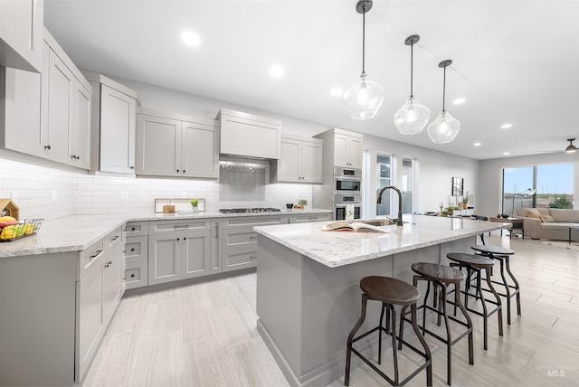 kitchen featuring decorative backsplash, light stone counters, appliances with stainless steel finishes, gray cabinets, and a kitchen bar