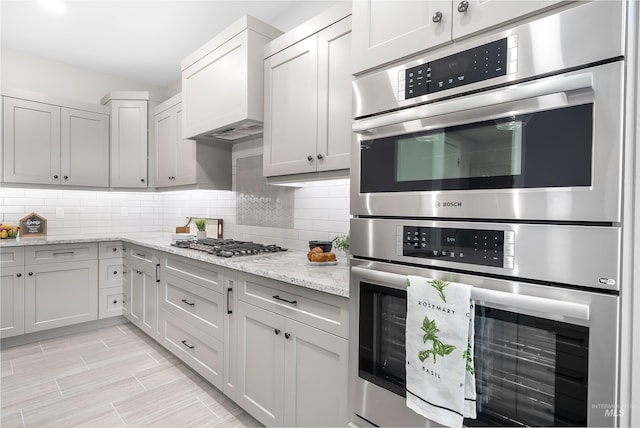 kitchen featuring stainless steel appliances, backsplash, wood tiled floor, light stone countertops, and premium range hood