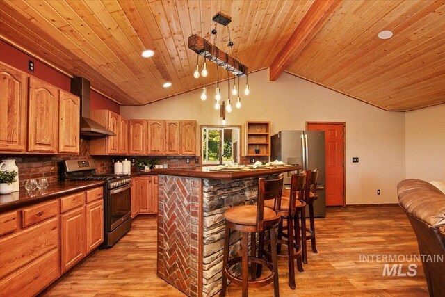 kitchen with light wood-type flooring, lofted ceiling with beams, dark countertops, wall chimney exhaust hood, and stainless steel appliances