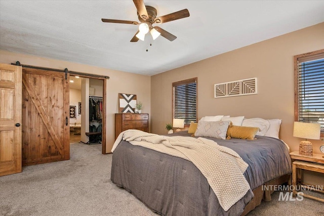 bedroom featuring a closet, a ceiling fan, a spacious closet, a barn door, and light carpet