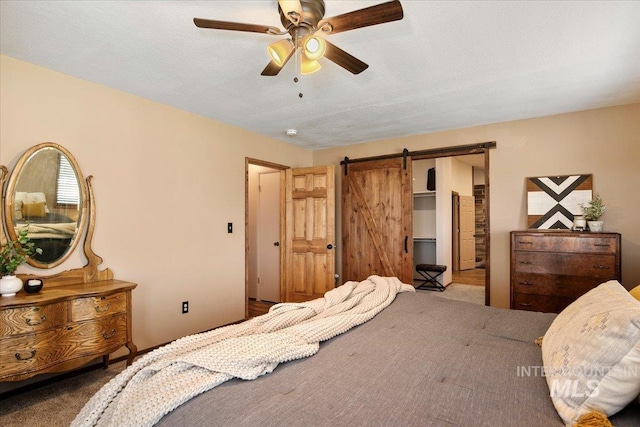 carpeted bedroom with ceiling fan, a walk in closet, and a barn door