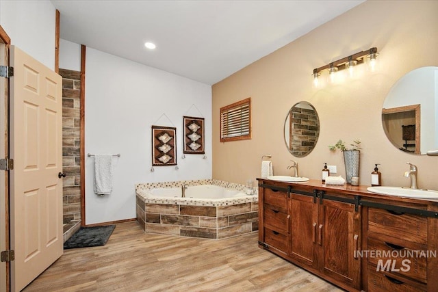 full bathroom featuring wood finished floors, double vanity, a sink, and a garden tub