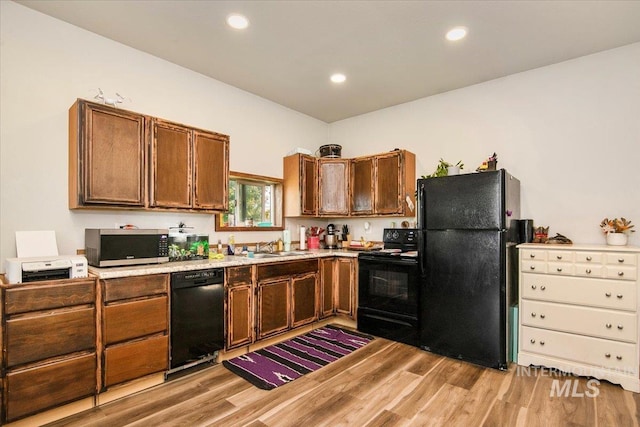 kitchen with a sink, light wood finished floors, light countertops, and black appliances