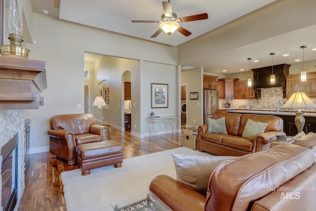 living area with ceiling fan, a fireplace, arched walkways, and wood finished floors