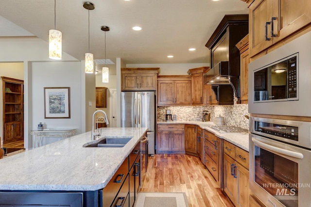 kitchen with tasteful backsplash, appliances with stainless steel finishes, a sink, an island with sink, and light stone countertops