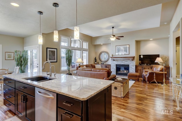 kitchen featuring dark brown cabinetry, light wood-style flooring, hanging light fixtures, a fireplace, and a sink