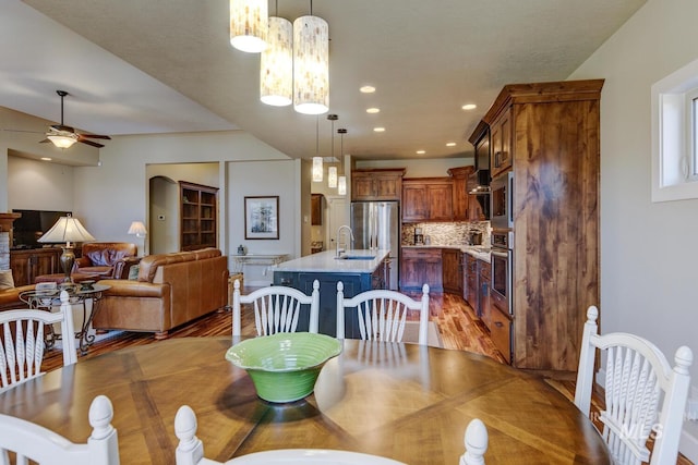 dining area with ceiling fan with notable chandelier, light wood finished floors, arched walkways, and recessed lighting