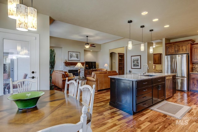 kitchen featuring arched walkways, a stone fireplace, light wood-style flooring, stainless steel appliances, and a sink