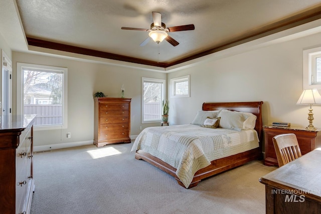 bedroom featuring light carpet, baseboards, a raised ceiling, and a ceiling fan