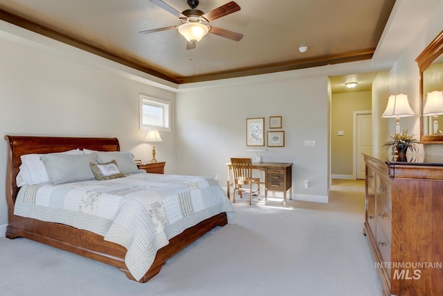 bedroom featuring light carpet, baseboards, a tray ceiling, and ceiling fan