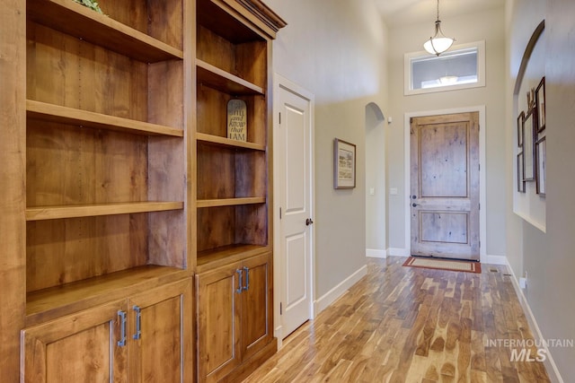 foyer with a towering ceiling, baseboards, arched walkways, and wood finished floors