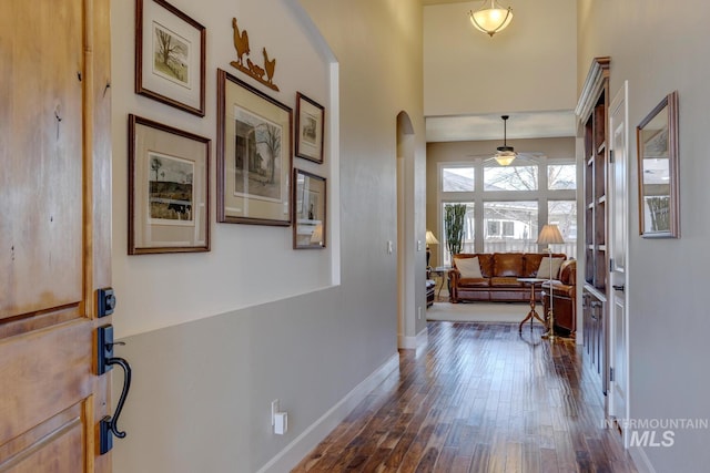 entryway with arched walkways, ceiling fan, dark wood-type flooring, and baseboards