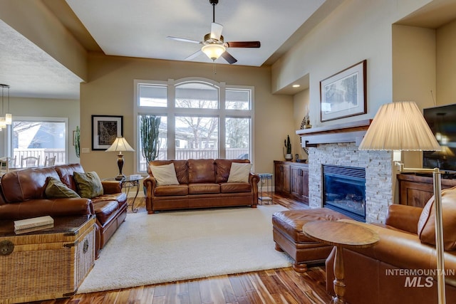 living area with a fireplace, wood finished floors, and a ceiling fan