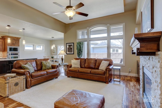 living room featuring ceiling fan, a fireplace, baseboards, and wood finished floors