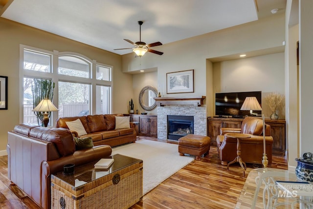 living area with ceiling fan, a stone fireplace, and wood finished floors