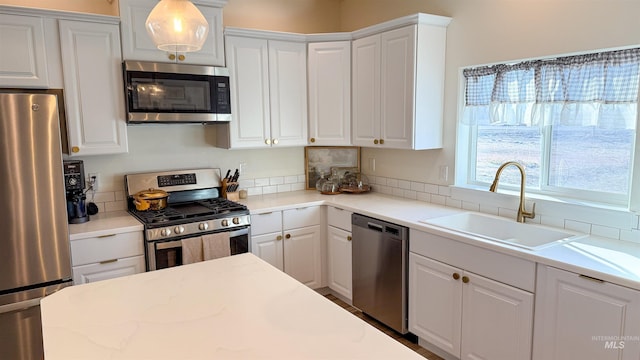 kitchen with pendant lighting, appliances with stainless steel finishes, sink, and white cabinets