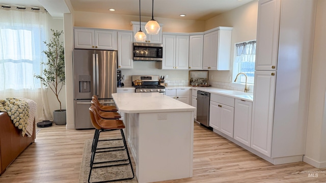 kitchen featuring decorative light fixtures, white cabinetry, sink, a center island, and stainless steel appliances