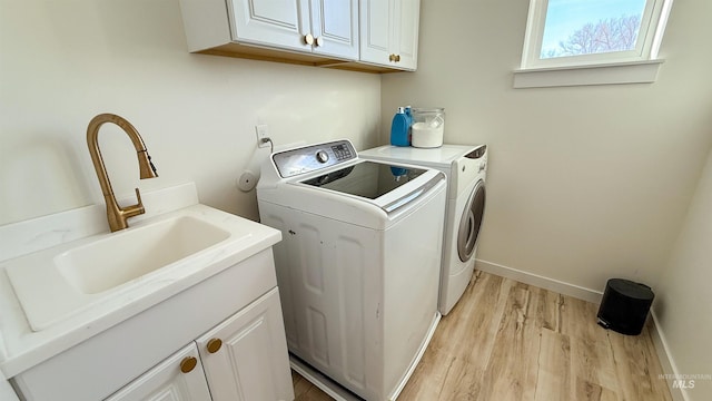 clothes washing area with sink, cabinets, washing machine and clothes dryer, and light wood-type flooring