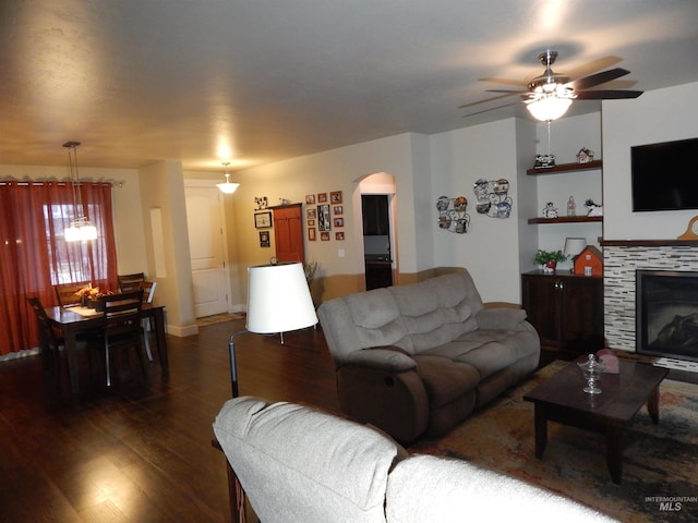 living room featuring dark wood-type flooring, ceiling fan, a tiled fireplace, and built in features