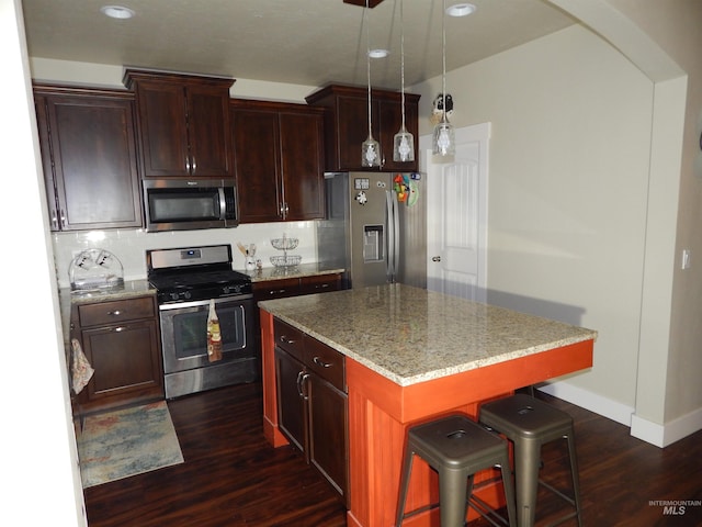 kitchen featuring dark wood-type flooring, appliances with stainless steel finishes, a kitchen island, light stone countertops, and a kitchen bar