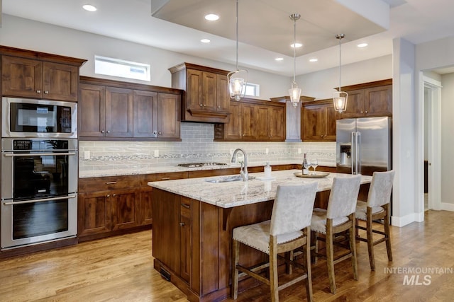 kitchen featuring pendant lighting, sink, a kitchen island with sink, stainless steel appliances, and light stone countertops